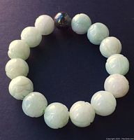Carved pale green Nephrite jade bracelet with one dark hematite bead on a dark background showing round carved beads.