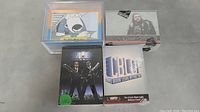 Photo showing four sets of trading cards: Family Guy cards stacked in a clear plastic case, Game of Thrones boxed set with character image, Men In Black boxed set with two agents, and CBLDF boxed set.