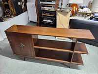 Front side view of wooden bookshelf TV stand showing cabinet door with metal decorative handle and open shelves.