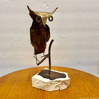 Front angle view of metal owl sculpture with visible textured and oxidized metal surface, mounted on white stone base