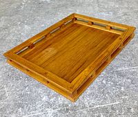 Angled view of the teak serving tray showing the raised edges with cut-out grips and wood grain pattern.
