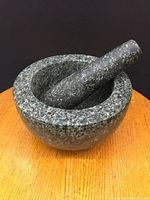 Granite mortar and pestle set shown on wooden surface against black background.