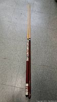Two detachable pool cues laid on a floor, one with reddish-brown finish and decorative grip, the other with plain light wood, both two-piece cues.