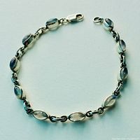 Full view of the sterling silver bracelet showing the linked oval bezels each with a polished moonstone and the lobster clasp closure