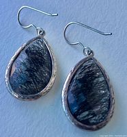 Pair of sterling silver earrings with black rutile quartz teardrop gemstones, displayed on a flat surface with natural lighting.