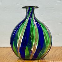 Front view of round Murano glass vase with blue, green, and gold aventurine stripes on wooden surface.