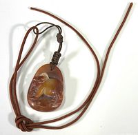 Full view of brown carved stone pendant with animal figure and brown cord laid flat