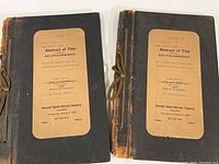 Two large bound volumes with string bindings and labels on front covers detailing abstract of title and list of incumbrances dated April 7, 1909. Covers show wear.