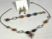 Photo showing the full set of jewelry: necklace, bracelet, and earrings, placed on a flat surface with visible detail of polished stones and wire wrapping.