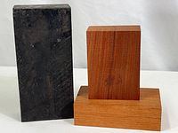 Three wood blocks arranged on white surface, largest black block and two reddish blocks stacked