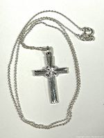 Sterling silver chain laid out with clasp visible and attached cross pendant in center.