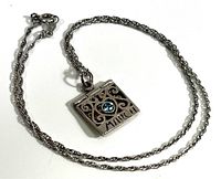 Full view of silver chain with attached rectangular pendant featuring scroll designs and blue stone.