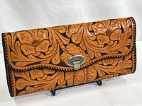 Front view of rectangular leather handbag with intricate hand tooled floral patterns and metal clasp