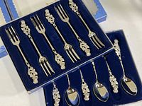 Six silverplate dessert spoons with raised rose pattern on handles, housed in original blue velvet-lined box; classic rounded bowls approx. 5-1/4 inches long.