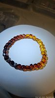Top view of the AAA Baltic amber stretchy bracelet showcasing the gradient colors of the polished beads from dark brown to honey yellow on white background.