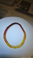 Photo of the AAA Baltic amber bracelet arranged in a circle showing beads transitioning from dark red and orange to yellow under white light.