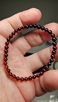 Close-up photo of a deep red Baltic amber bead stretchy bracelet, showing the translucent round beads held in hand.