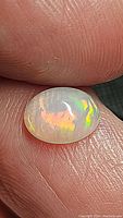 Close-up photo of an oval cabochon Ethiopian opal held between fingers showing vibrant fire and color play.