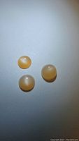 Three round cabochon peach moonstones arranged in a triangle on white background showing their color and cat's eye flash effect