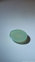 Oval cabochon chalcedony gemstone on white background showing color and shape under ambient light