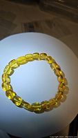 Top view of chunky natural golden Baltic amber bead bracelet arranged in a circle on a white surface with shadowing to highlight bead clarity and color.