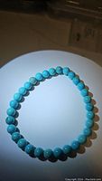 Photo of a stretchy bracelet with smooth, round robin's egg blue turquoise beads arranged in a circle on a white surface.