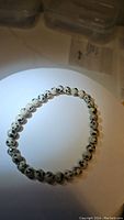 Natural dalmatian jasper bracelet on a light surface, showing round spotted beads in a circle.