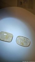 Two rectangular rounded natural rutilated quartz gemstones with golden needle inclusions under spotlight, showing clarity and internal inclusions.