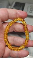 Close-up photo of a stretchy bracelet made of small, disk-shaped golden Baltic amber beads held between fingers.