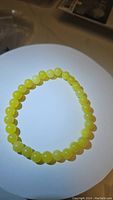 Photo of a lemon jade bead bracelet arranged in a circle on a white background. Shows smooth round yellow-green beads.