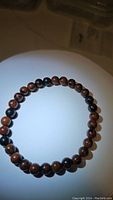 Top view of stretchy mahogany jasper bead bracelet laid flat on a white circular display with light illuminating beads, showing brown and reddish tones with patterns.