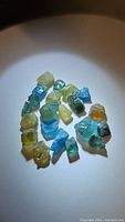 Collection of multicolored rough apatite crystals displayed on a light surface under direct light, showcasing vibrant hues of blue, green, and yellow