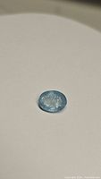 Oval cut light blue aquamarine gemstone with visible inclusions, laying flat on a white surface.