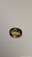 Close-up photo of an oval cut golden champagne citrine gemstone on a plain background.