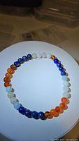Photo showing natural gemstone bracelet comprised of blue Lapis Lazuli, white Jade, amber-hued Baltic Amber, and red-orange Agate beads arranged in a circular layout.