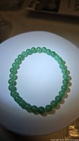 Top-down photo of circular green aventurine bead bracelet on white circular platform, showing uniform bead sizes and color.