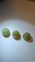Three natural mossy green aventurine gemstones, bullet cut, placed under a light source showing their color and smooth dome shape.