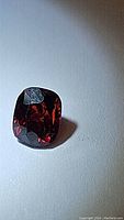 Close-up photo of cushion cut deep red spinel gemstone showing facets and color under natural light.