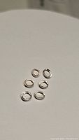 Close-up photo of six smooth silver jump rings arranged on a neutral background, used for jewelry making.