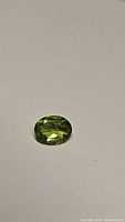 Close-up photo of a natural apple green peridot gemstone, oval cut, lying on a plain surface.