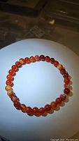 Photo of circular stretchy bracelet made of polished natural red agate beads with visible natural banding and swirls, approx 6mm size, arranged on a white background and lit to highlight bead patterns.