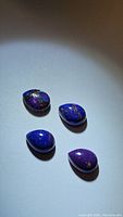 Four pear cabochon purple copper turquoise gemstones with visible copper matrix under bright lighting.