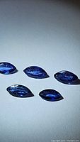 Five royal blue marquis cut sapphires arranged on a white surface, showing the color and faceting details