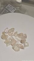 Photo showing 15 small natural rough untreated morganite crystals in soft pink and peach shades on a white background.