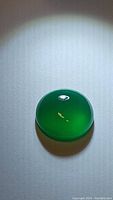 Photo of round vivid green onyx gemstone showing smooth domed cabochon surface and rich green color with light reflection.