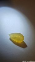 Pear-shaped yellow opal gemstone under spotlight showing translucent yellow color and smooth glossy surface.