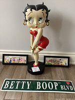 Full view of the Betty Boop figurine on base with two framed comic strips behind and sign in front