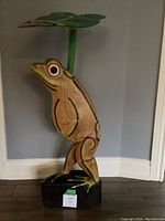 Front view of wooden frog sculpture holding water lily leaf, showing size and condition.