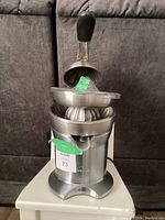 Front view of the Breville stainless steel citrus juicer assembled with the cone and strainer on top, black rubber lever handle visible