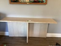 Front view of natural stone console table with smooth flat top and two vertical support panels placed on wooden floor against wall.
